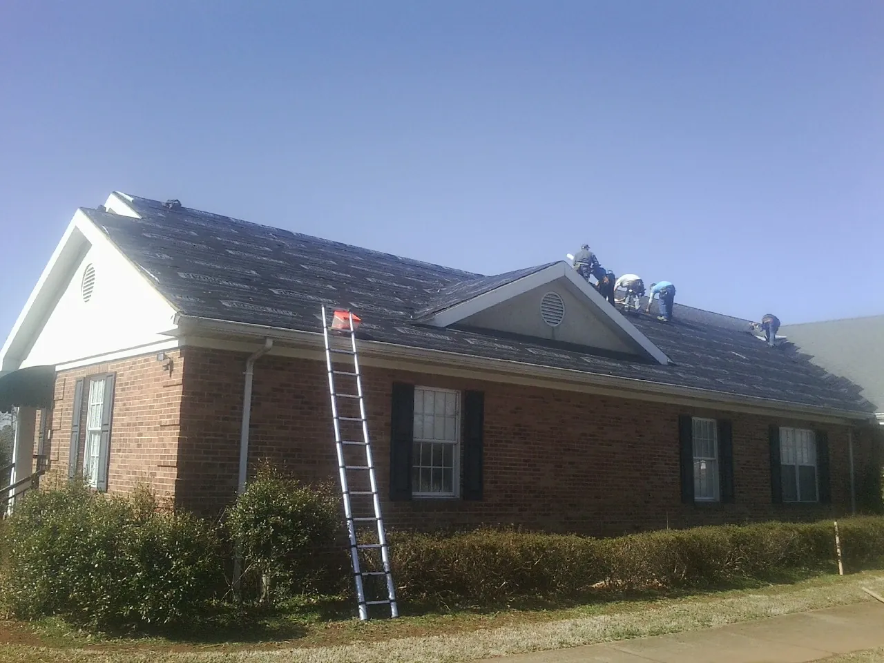 Crew tearing shingles off a brick ranch roof with a ladder set — Metal Roof Repair work by our crew in Schaumburg