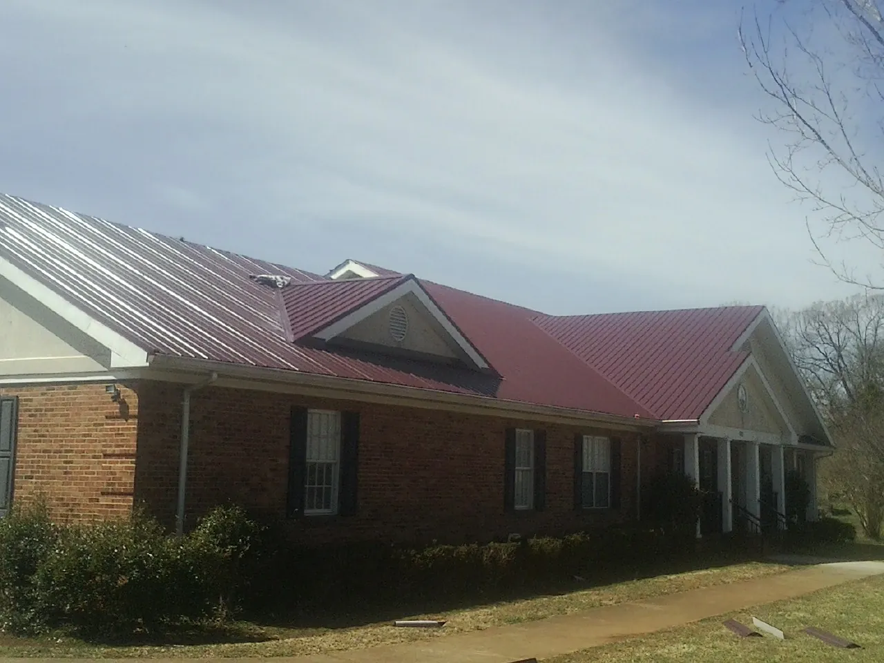 Red metal roof with gabled entries on a long brick building, from a Hail Damage Roof Repair job in Schaumburg