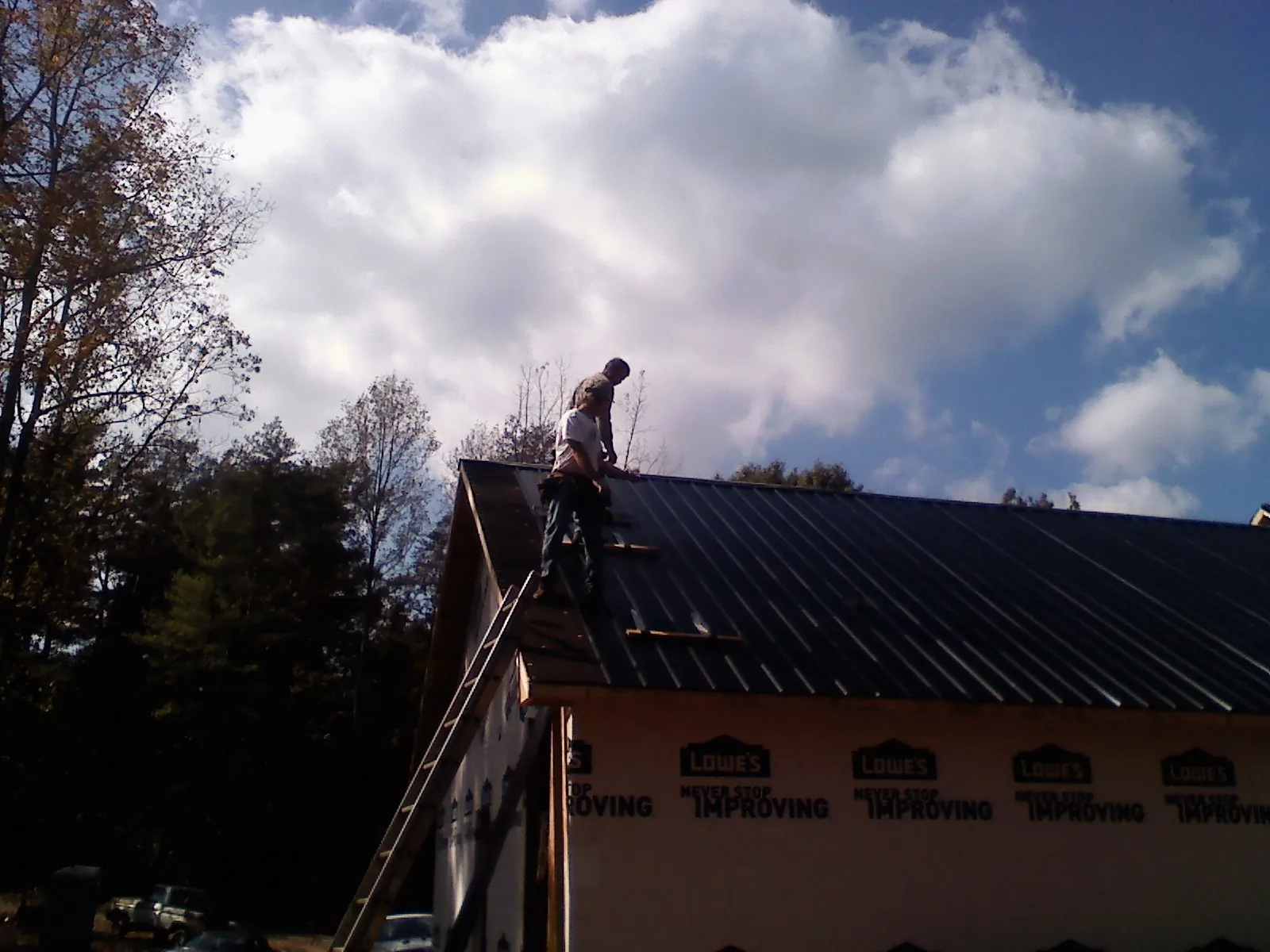 Roofer fastening dark metal panels high against a cloudy sky, from a Roof Inspection job in Schaumburg