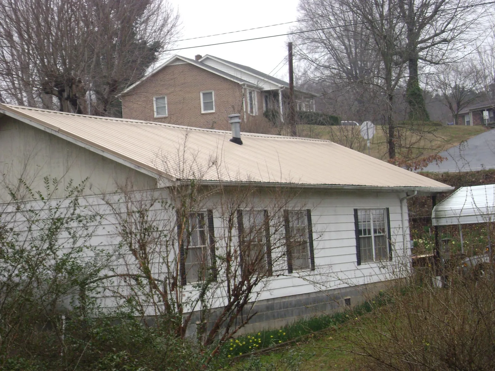 Tan metal roof on a white sided house set into a hillside — Commercial Roofing by Roofing Brothers in Schaumburg